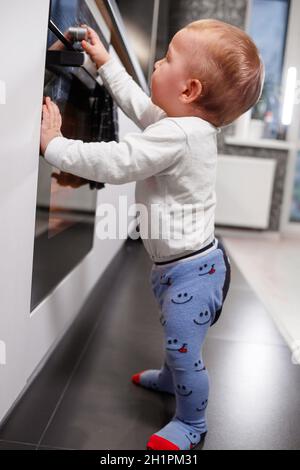 Petit enfant jouant avec cuisinière électrique dans la cuisine Banque D'Images