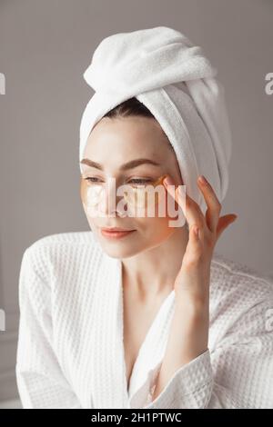 Jolie fille européenne appliquant des patchs de collagène doré sous ses yeux. Femme traitement du visage. Cosmétologie, beauté et spa Banque D'Images