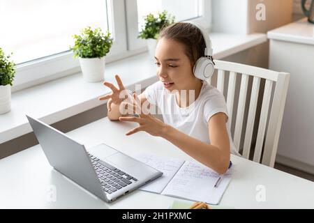 Concept d'éducation en ligne - élève fille dans un casque blanc devant un moniteur d'ordinateur portable parler avec un enseignant pendant une leçon en ligne. Banque D'Images