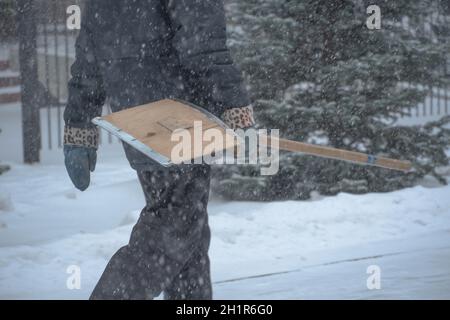 Un homme en activité du service municipal avec une pelle à neige marche le long de la route dans une tempête, un blizzard ou une chute de neige en hiver par mauvais temps dans la ville.E Banque D'Images