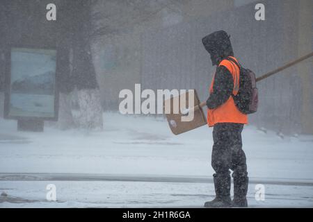 Un homme en activité du service municipal avec une pelle à neige marche le long de la route dans une tempête, un blizzard ou une chute de neige en hiver par mauvais temps dans la ville.E Banque D'Images