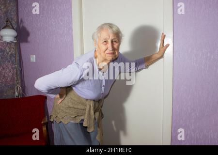 Femme âgée de 75s avec des sentiments douloureux massant bas de dos pour réduire la douleur, mal de dos inconfort.Maladies des personnes âgées, lésion du nerf sciatique Banque D'Images