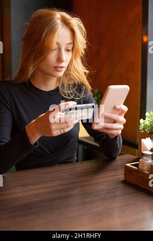Jeune femme effectuant le paiement par carte par téléphone portable pour payer des factures.Photo verticale. Banque D'Images