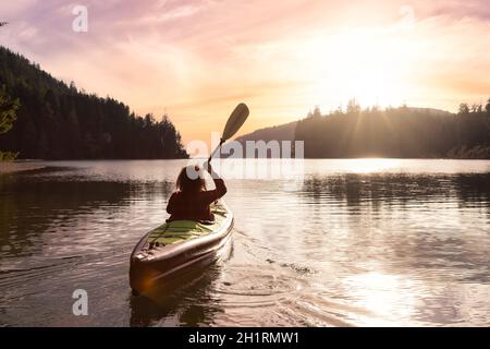 Une fille aventureuse qui fait du kayak dans l'océan Pacifique. Rendu d'art du ciel du coucher du soleil. Prise à San Josef Bay, Cape Scott, dans le nord de l'île de Vancouver, en Colombie-Britannique Banque D'Images