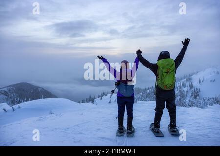 North Vancouver, Colombie-Britannique, Canada - 13 février 2021 : couple aventureux au sommet de Seymour Mountain pendant le coucher du soleil hivernal enneigé. Banque D'Images