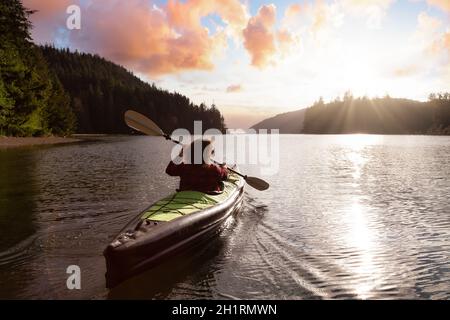 Une fille aventureuse qui fait du kayak dans l'océan Pacifique. Rendu d'art du ciel du coucher du soleil. Prise à San Josef Bay, Cape Scott, dans le nord de l'île de Vancouver, en Colombie-Britannique Banque D'Images