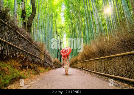 Femme dans la Yukata traditionnelle avec parapluie rouge à la forêt de bambou d'Arashiyama à Kyoto, Japon Banque D'Images