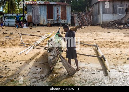 Ambatozavavy, Nosy Be, Madagascar - Le 19 décembre 2015 : batelier et sa pirogue en bois traditionnel avec outrigger dans le village de pêche Ambatozavavy sur Banque D'Images