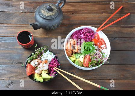 Aliments biologiques. Recette de fruits de mer frais. Deux poke-bols frais avec saumon, crevettes, riz, chou rouge, avocat, tomates cerises et pousses de radis sur la terre de courge Banque D'Images