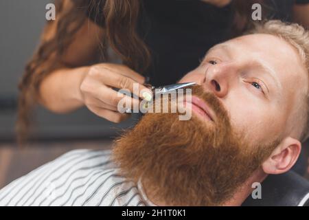 Un homme dans un salon de coiffure. Femme barbier tachant la moustache. Femme de coiffure dans le masque Banque D'Images