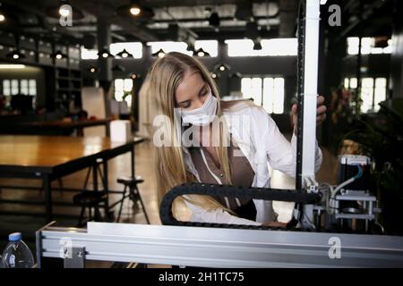 Jeune femme souriante analysant une partie de machine au cours de son expérience scientifique en laboratoire. Banque D'Images