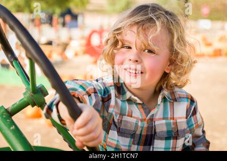 Adorable jeune garçon jouant sur un vieux tracteur dans un cadre rustique de l'automne en plein air. Banque D'Images