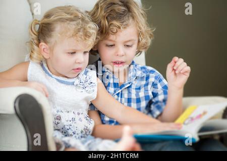 Jolies jeunes frère et Sœur de lire un livre ensemble dans une chaise. Banque D'Images