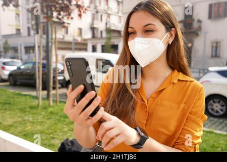 Portrait d'une belle jeune femme portant un masque de protection KN95 FFP2 appels vidéo avec un téléphone mobile à l'extérieur Banque D'Images