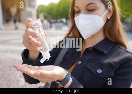 Gros plan de la belle jeune femme portant un masque de protection KN95 FFP2 en utilisant du gel d'alcool aseptisant ses mains dans la rue de la ville. Concentrez-vous sur les mains. Banque D'Images