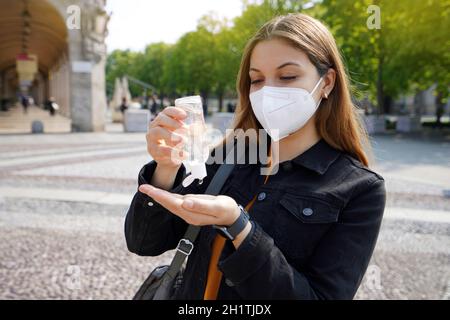 Portrait d'une belle jeune femme portant un masque de protection KN95 FFP2 en utilisant du gel d'alcool aseptisant ses mains dans la rue de la ville. Hygiène et soins de santé con Banque D'Images