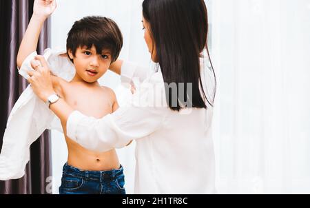 Asiatique bonne belle mère aidant à obtenir des vêtements habillés sur son garçon enfant dans la maison pour prêt avant d'aller à l'école, concept de retour à l'école Banque D'Images