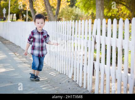 Cute Young Mixed Race Boy Walking Stick avec le long de clôture blanche. Banque D'Images