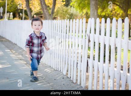 Cute Young Mixed Race Boy Walking Stick avec le long de clôture blanche. Banque D'Images