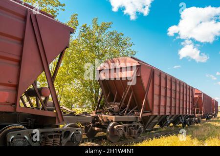 Conteneurs ferroviaires avec matériaux en vrac. La locomotive tire un grand train de marchandises. Jour ensoleillé d'été. Banque D'Images