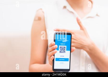 Jeune femme asiatique pointant vers du plâtre adhésif sur le bras elle a vacciné et montrant l'application smartphone écran numérique mobile vacciné coronavirus (COVID-19 Banque D'Images