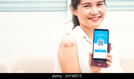 La jeune femme asiatique sourit a un pansement adhésif sur le bras qu'elle a vacciné et montrant l'application smartphone écran numérique mobile coronavirus vacciné (COVID-19) Banque D'Images