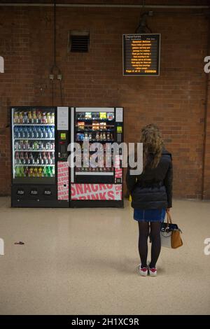 Doncaster, Royaume-Uni, 22 mai 2021: Le tableau des départs affiche les informations COVID pour les voyages en train, lues par une jeune femme debout par des distributeurs automatiques Banque D'Images