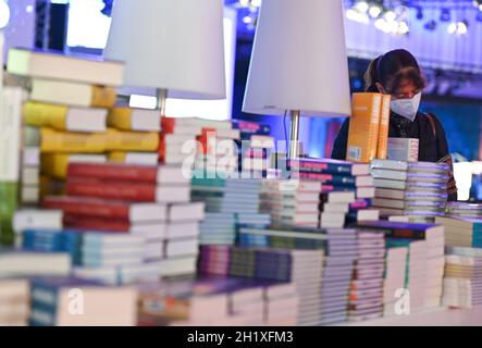 19 octobre 2021, Hessen, Francfort-sur-le-main : une femme se tient à côté d'une pile de livres sur la touche de la conférence de presse d'ouverture de la Foire du livre à la Festhalle.Le pays invité de cette année est le Canada.Photo: Arne Dedert/dpa Banque D'Images