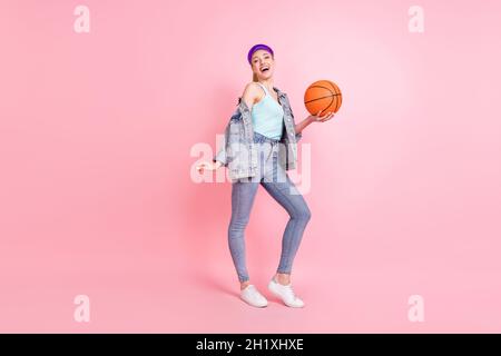 Photo de tout le corps de blonde funky femme millénaire jouer basket-ball porter jeans veste visière isolée sur fond rose Banque D'Images