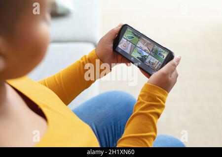 Femme afro-américaine de taille plus qui vérifie la vue des caméras de sécurité sur un smartphone Banque D'Images
