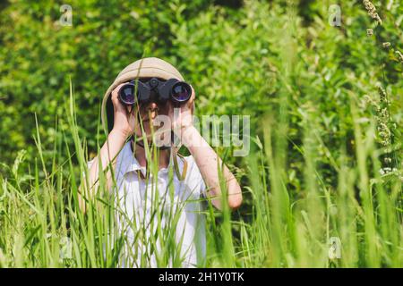 Préadolescence fille portant un casque de liège debout dans l'herbe regardant à travers des jumelles.Concept de découverte Banque D'Images