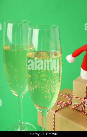 Verres de champagne, chapeau de père Noël et boîtes-cadeaux sur fond vert. Banque D'Images
