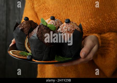 Femme en chandail tient une assiette avec des muffins, gros plan. Banque D'Images