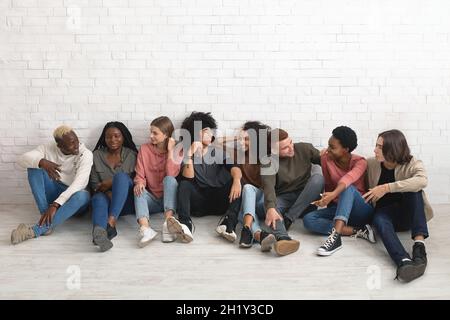 Les jeunes du millénaire multiraciaux se rafraîchient ensemble, assis sur le sol Banque D'Images