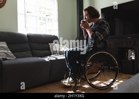 Homme caucasien attentionné assis sur un fauteuil roulant pour boire du café à la maison Banque D'Images