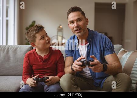 Le père et le fils caucasiens jouant ensemble des jeux vidéo assis sur le canapé à la maison Banque D'Images