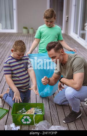 Un père caucasien et deux fils collectent des matières plastiques dans un sac à l'extérieur Banque D'Images