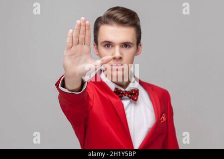 Arrêter.Portrait d'un gentleman confiant avec une coiffure élégante en smoking rouge et noeud papillon montrant le geste de la main de prohibition, dire non, interdit, refuser concept. Studio en intérieur tourné isolé, fond gris Banque D'Images