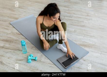 Jeune femme indienne regardant des vidéos sportives en ligne sur un ordinateur portable avant l'entraînement à la maison, au-dessus de la vue Banque D'Images