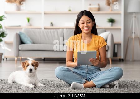 Jolie femme chinoise regardant le blog du propriétaire d'animal de compagnie sur une tablette numérique Banque D'Images