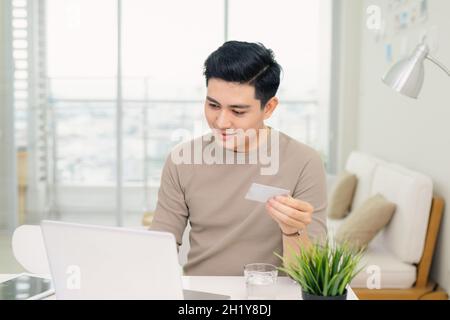 beau jeune homme d'affaires utilisant un ordinateur tout en tenant une carte de crédit dans un bureau à la maison Banque D'Images