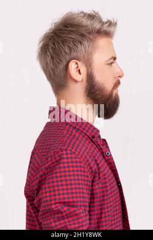 Portrait de profil d'un homme à barbe confiante avec des cheveux blonds portant une chemise à carreaux rouge regardant l'espace latéral avec un visage attentif sérieux.Prise de vue en studio isolée sur fond gris Banque D'Images