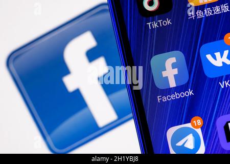 Icône de l'application de réseau social Facebook parmi d'autres applications sur l'écran du smartphone.En arrière-plan se trouve le logo Facebook. Banque D'Images