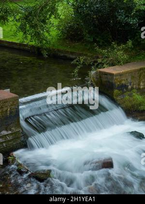 Une petite chute d'eau à plusieurs niveaux entourée d'un arbre dans un parc de banlieue, prise à l'aide d'un obturateur lent pour capturer la susurration de l'eau qui tombe. Banque D'Images