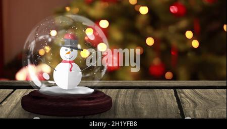Image du globe de neige avec bonhomme de neige sur une table en bois au-dessus de l'arbre de noël Banque D'Images