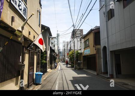 Une allée dans le centre-ville de Kyoto avec de petites maisons et le câble de réseau électrique.Drapeau national du Japon ou hinomaru sur l'une des maisons.Ciel bleu ciel nuageux. Banque D'Images