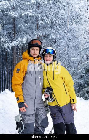 Portrait d'hiver de personnes heureuses d'origine caucasienne dans des casques et des lunettes de ski.Femme et son fils sur fond de forêt enneigée.Famille Banque D'Images