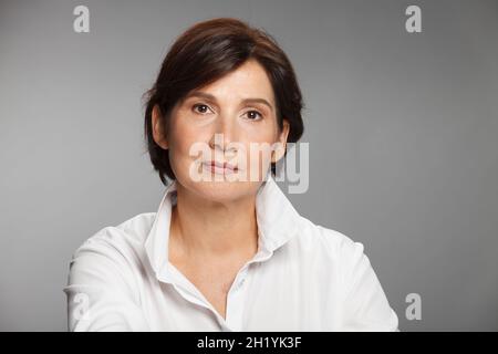 Portrait d'une femme d'âge moyen portant une chemise blanche sur fond gris Uni. Banque D'Images