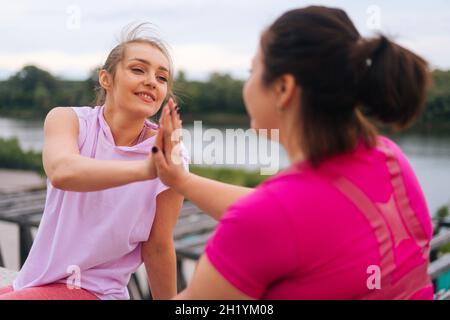 Vue rapprochée du dos de la forme physique positive femme entraîneur et motivé graisse jeune femme saluant les uns les autres avec les cinq élevés après l'exercice à l'extérieur Banque D'Images