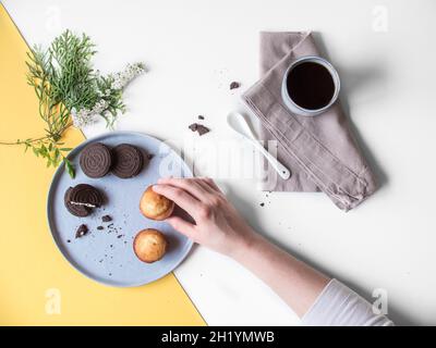 Une tasse de café à côté d'une main prenant un gâteau d'une assiette (vu d'en haut) Banque D'Images